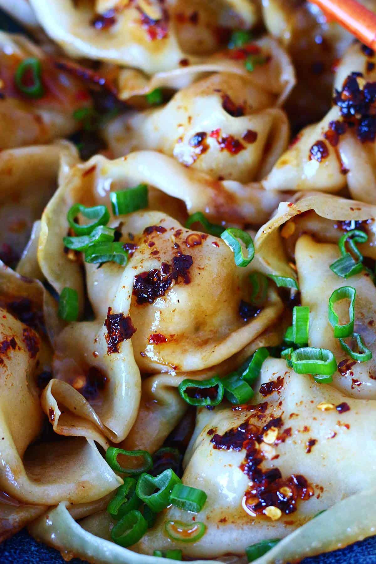 Close up of a plate of blanket dumplings with chili crisp and scallions.