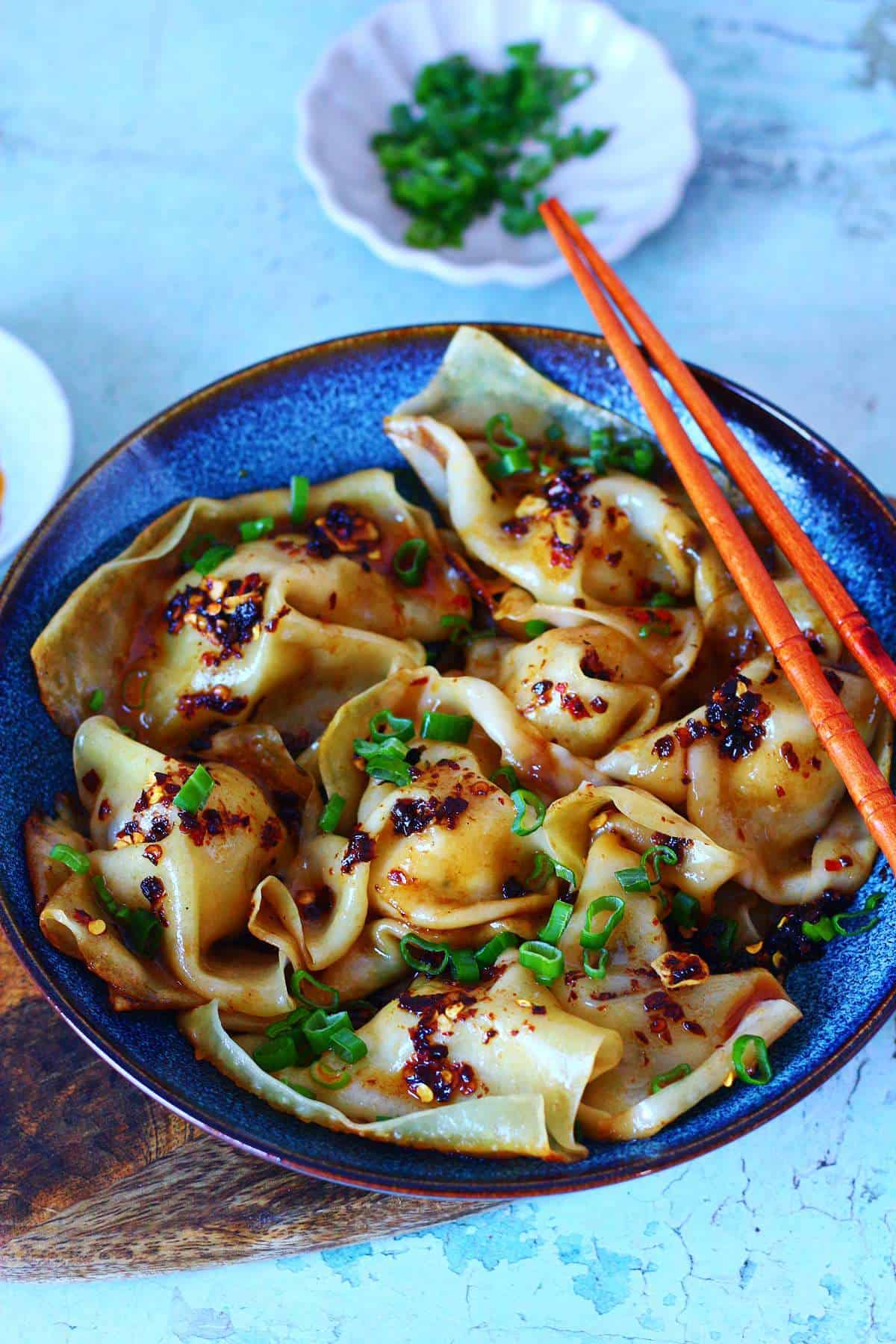 Bowl of dumplings with chili crisp and scallions, served with chopsticks.