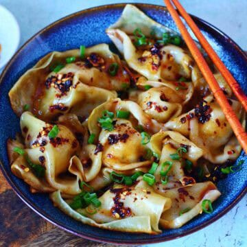 Blanket dumplings in a bowl topped with chili crisp and green onions.