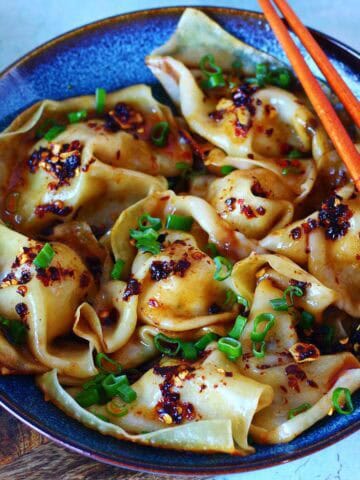 Blanket dumplings in a bowl topped with chili crisp and green onions.
