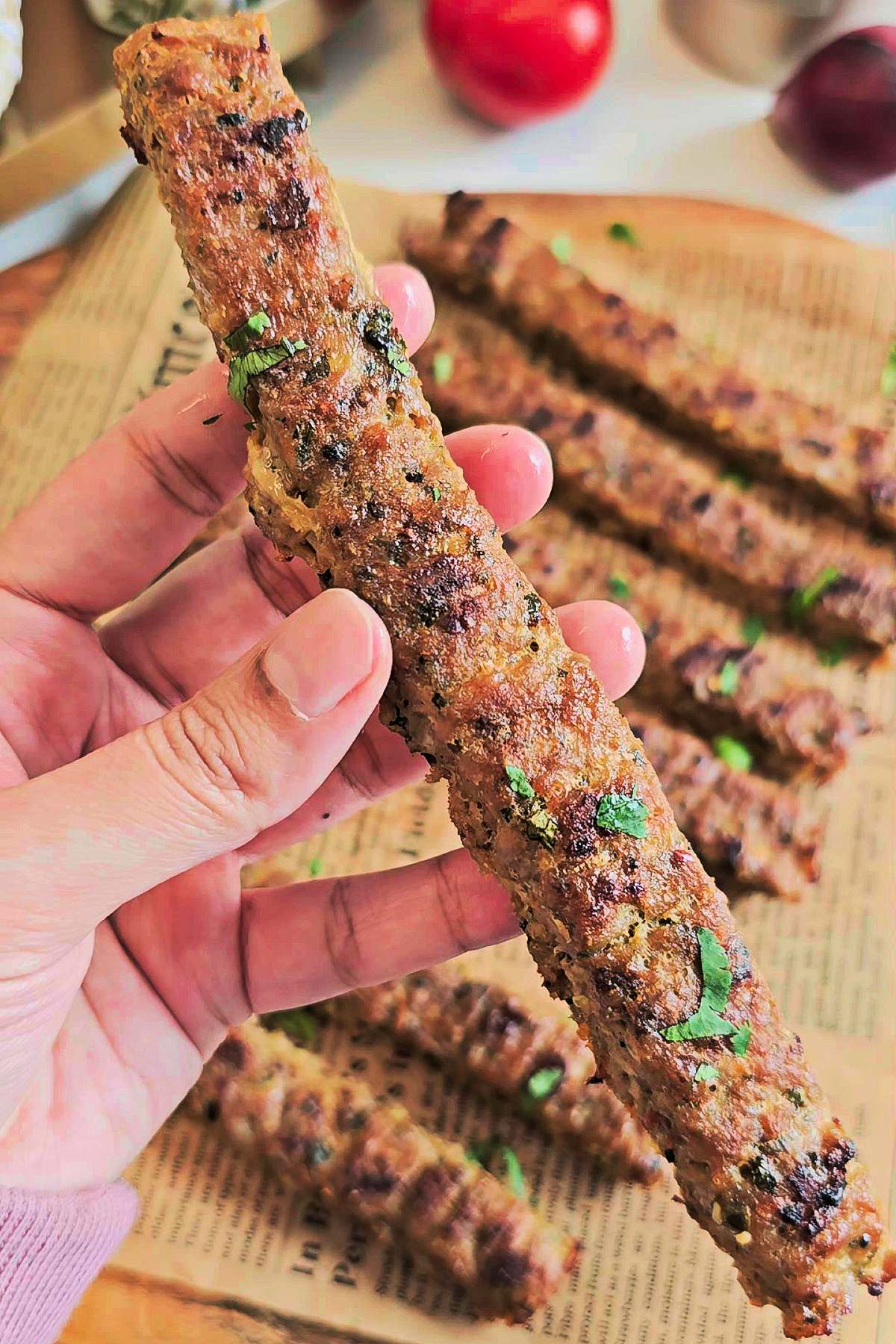 Holding a long kebab in hand with remaining kebabs in the background.