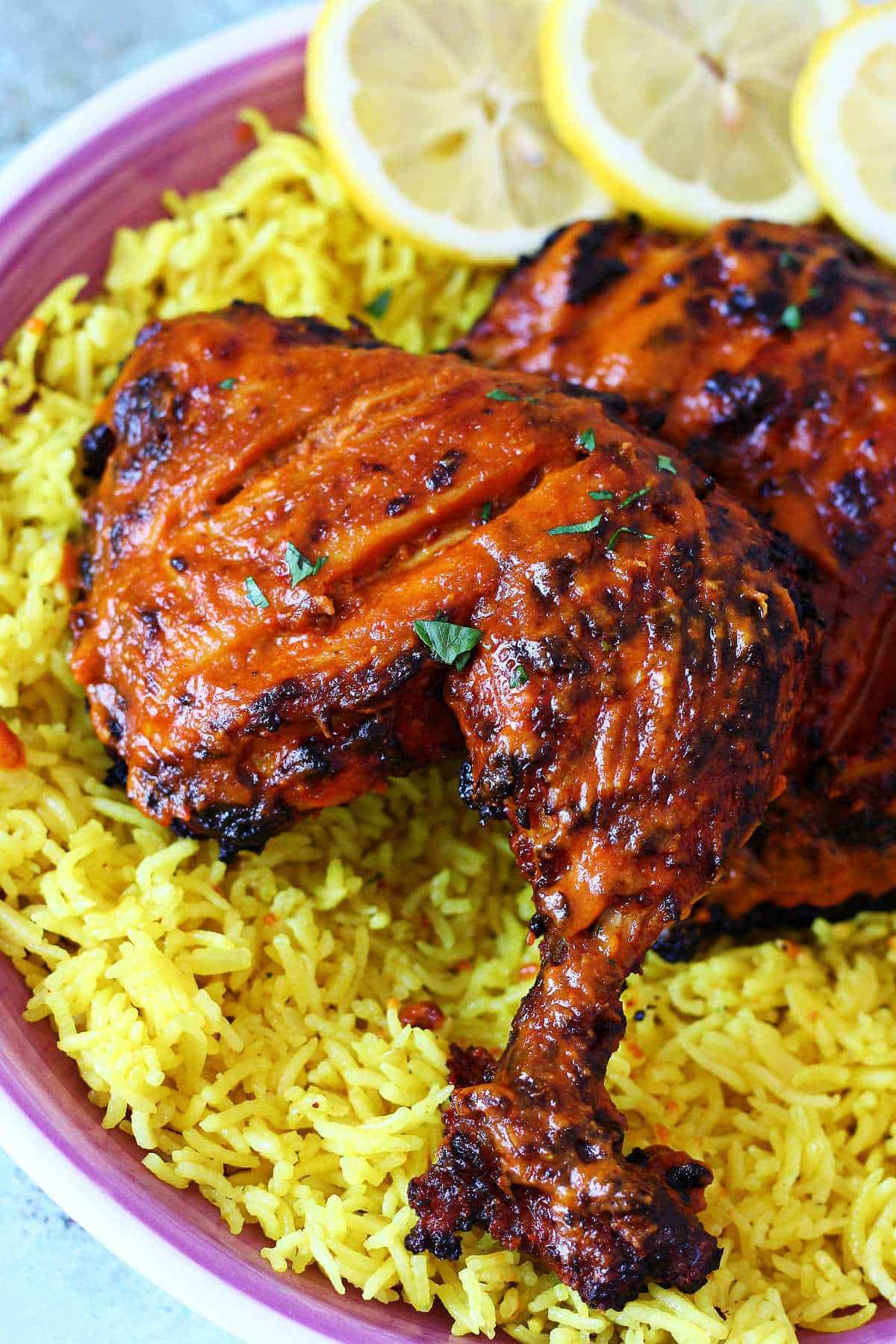 Close-up of charred peri peri chicken quarter served over yellow rice with lemon slices.