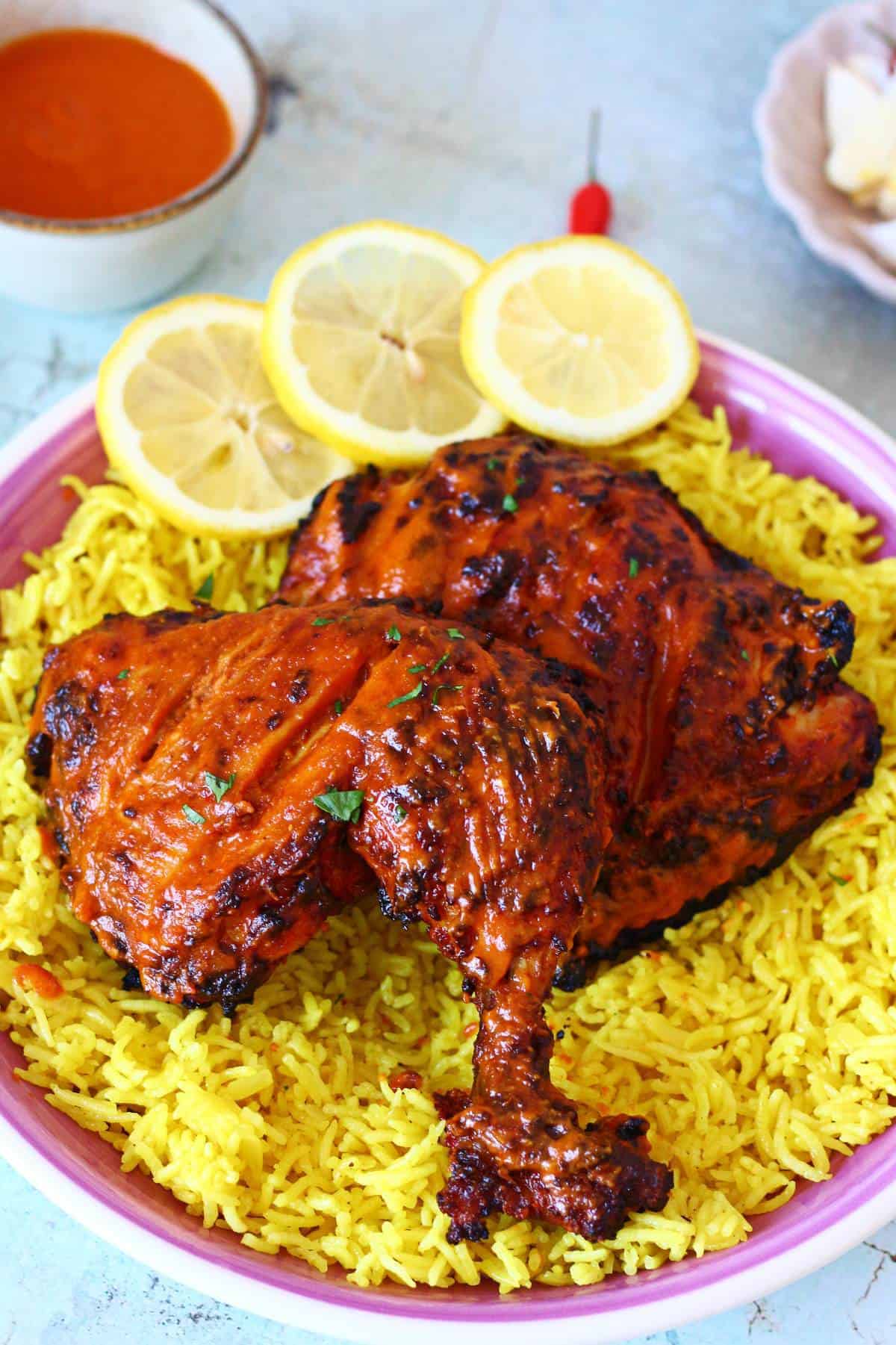 Nando’s-style peri peri chicken plated over yellow rice with lemon slices and peri peri sauce on the side.