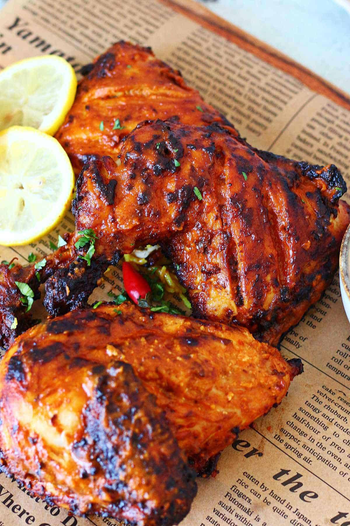 Charred peri peri chicken quarters served on brown parchment with lemon slices and dipping sauce.