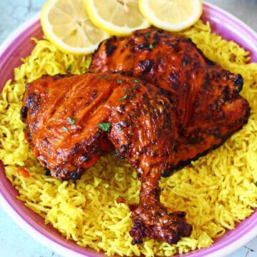 Peri peri chicken quarter served over yellow rice with lemon slices on a pink plate.