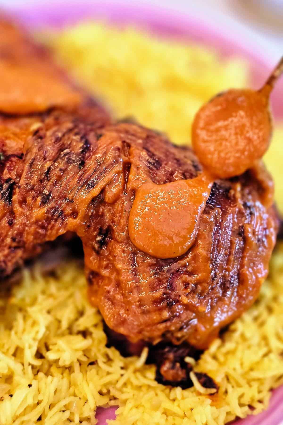 Spoon drizzling creamy peri peri sauce over charred peri peri chicken served with yellow rice.