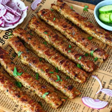Sheet pan kebabs arranged on parchment paper with sliced red onions and cucumbers on the side.