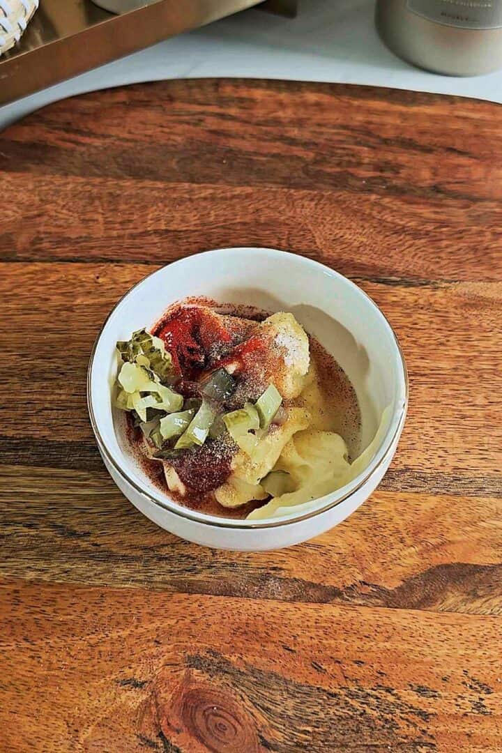 Big Mac sauce ingredients including mayonnaise, ketchup, mustard, chopped pickles, and spices in a small bowl on a wooden board.