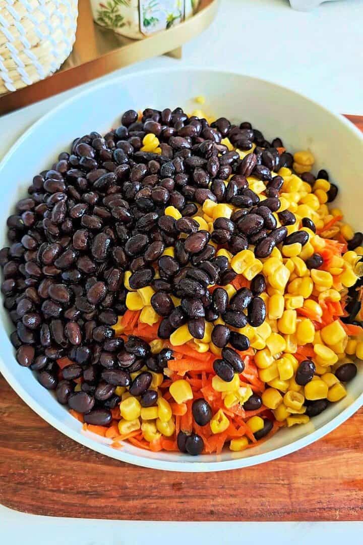 Unmixed bow tie pasta salad with black beans, peas, sweet corn, shredded carrots, and diced bell pepper in a large bowl.
