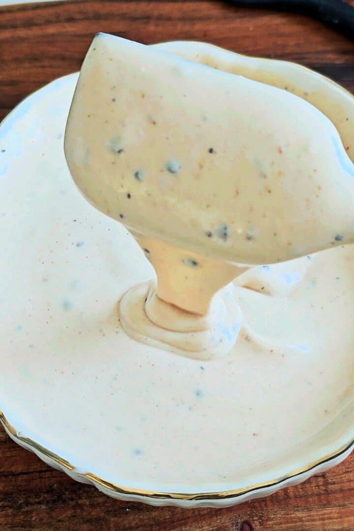 Creamy pasta salad dressing being poured from a spoon into a white bowl.