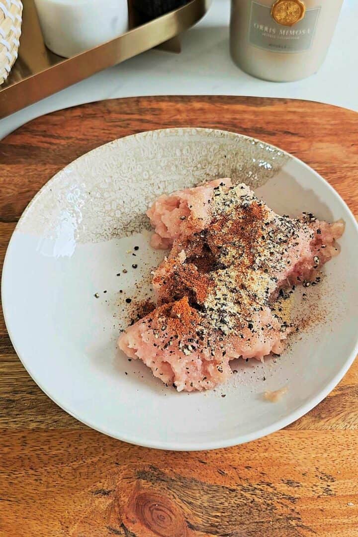 Ground chicken seasoned with garlic powder, paprika, black pepper, and spices in a shallow bowl.