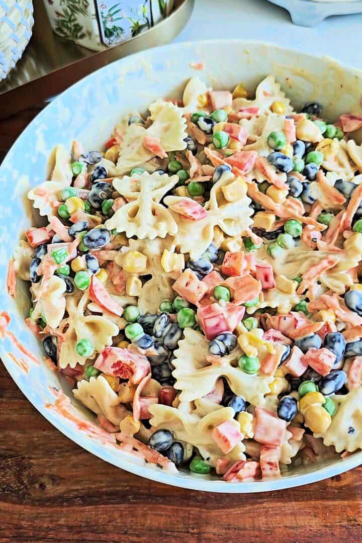 Creamy bow tie pasta salad mixed with black beans, peas, corn, carrots, and bell peppers in a large bowl.