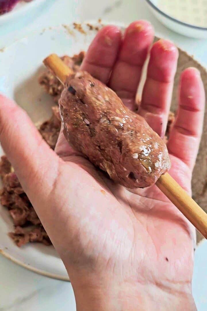 Hand shaping gola kabab mixture around a skewer.