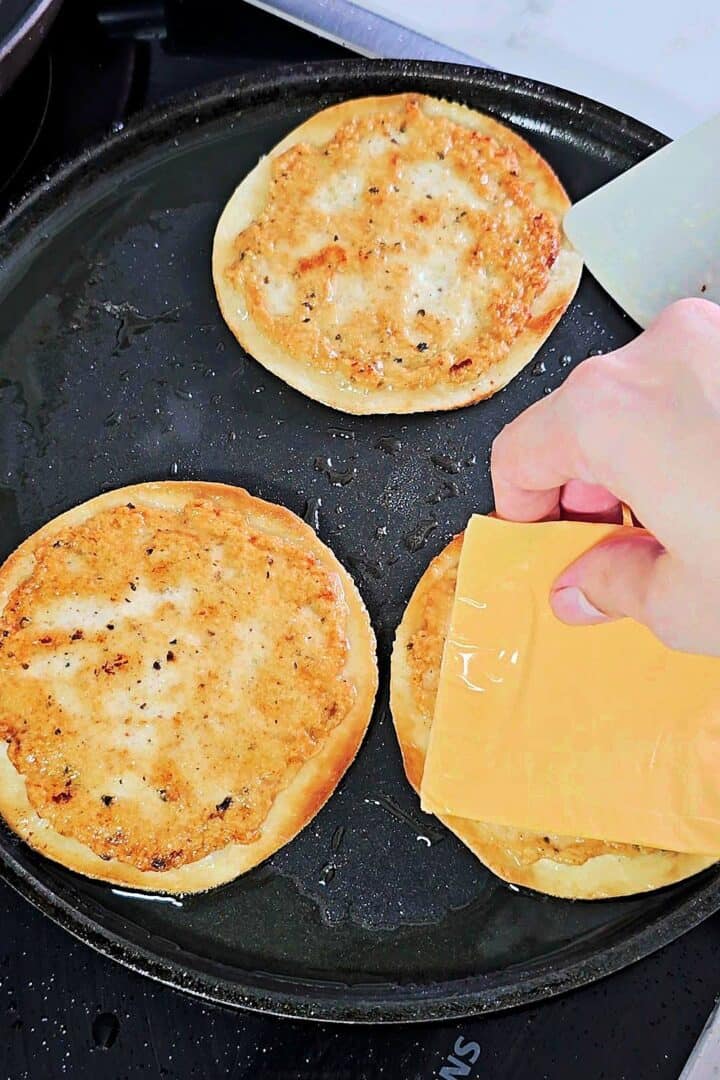 Slices of burger cheese being added to crispy chicken smash tacos in a skillet.