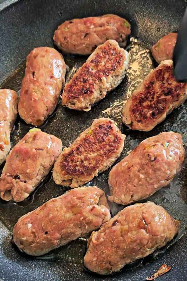 Gola kababs frying in a pan until browned and cooked through.
