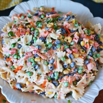 Creamy bow tie pasta salad served on a white plate with black beans, peas, sweet corn, carrots, and bell peppers.