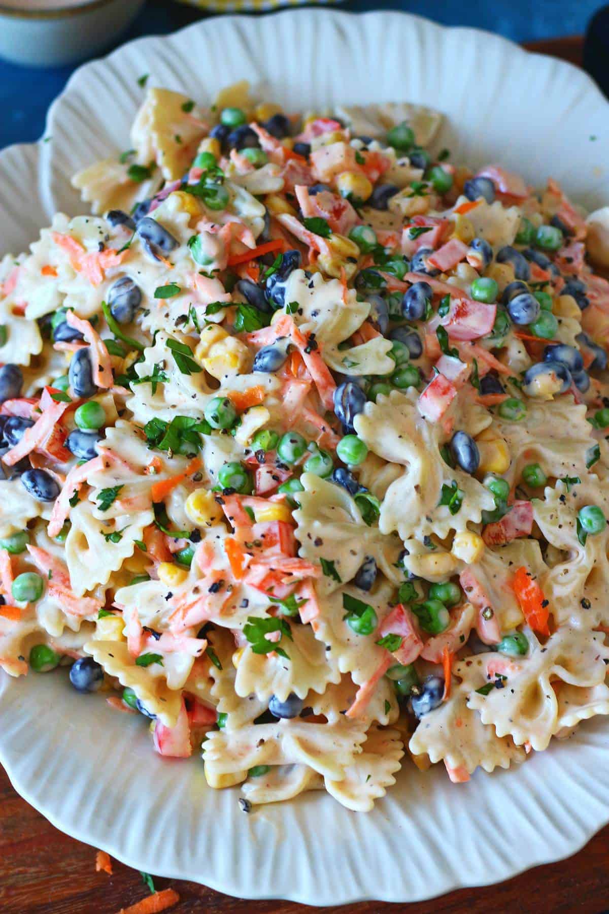 Creamy bow tie pasta salad garnished with herbs and cracked black pepper on a white serving plate.