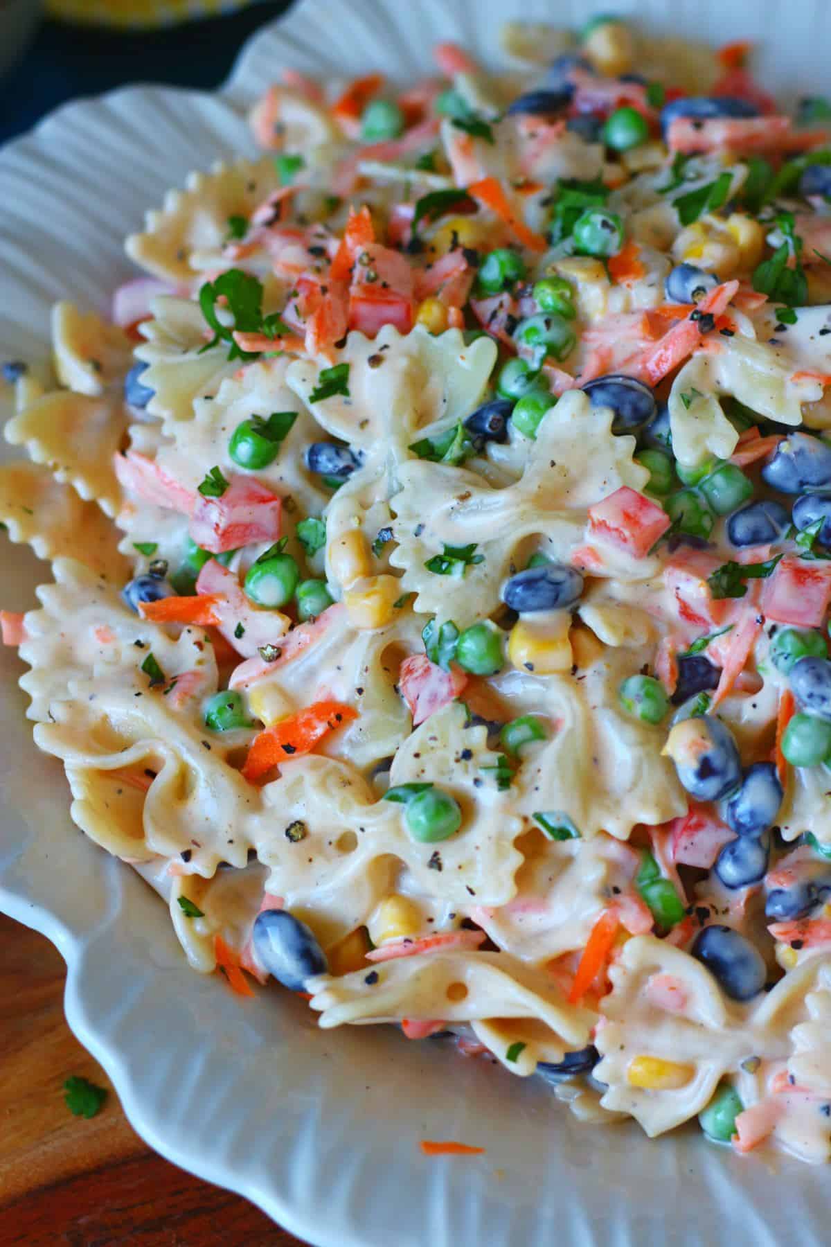 Close-up of creamy bow tie pasta salad with peas, black beans, corn, carrots, and bell peppers.