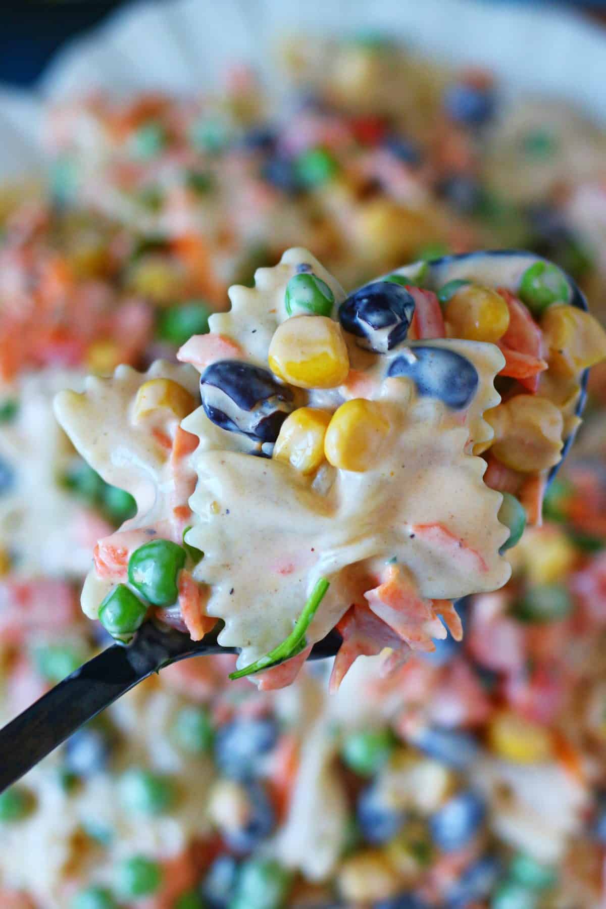 Spoonful of creamy bow tie pasta salad with black beans, peas, sweet corn, and carrots.