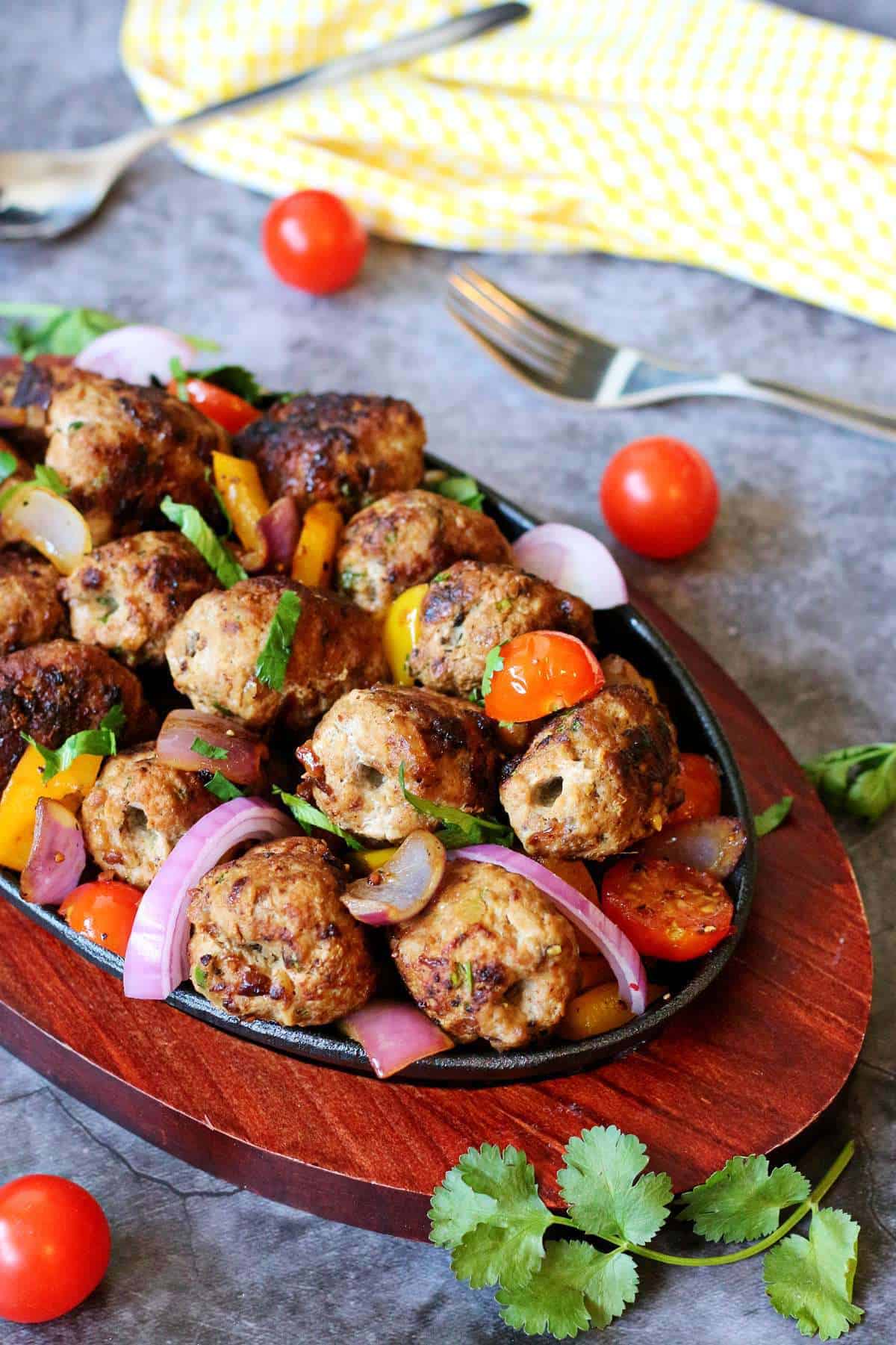 Gola kababs served in a cast iron skillet with cherry tomatoes, onions, bell peppers, and cilantro garnish.