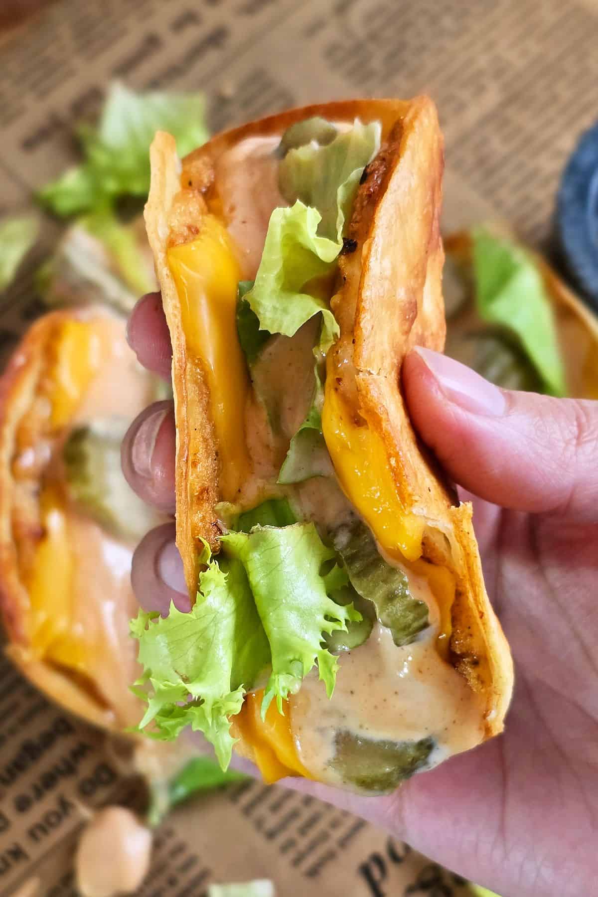 Hand holding a crispy Chicken Big Mac smash taco filled with melted cheese, lettuce, pickles, and creamy sauce.
