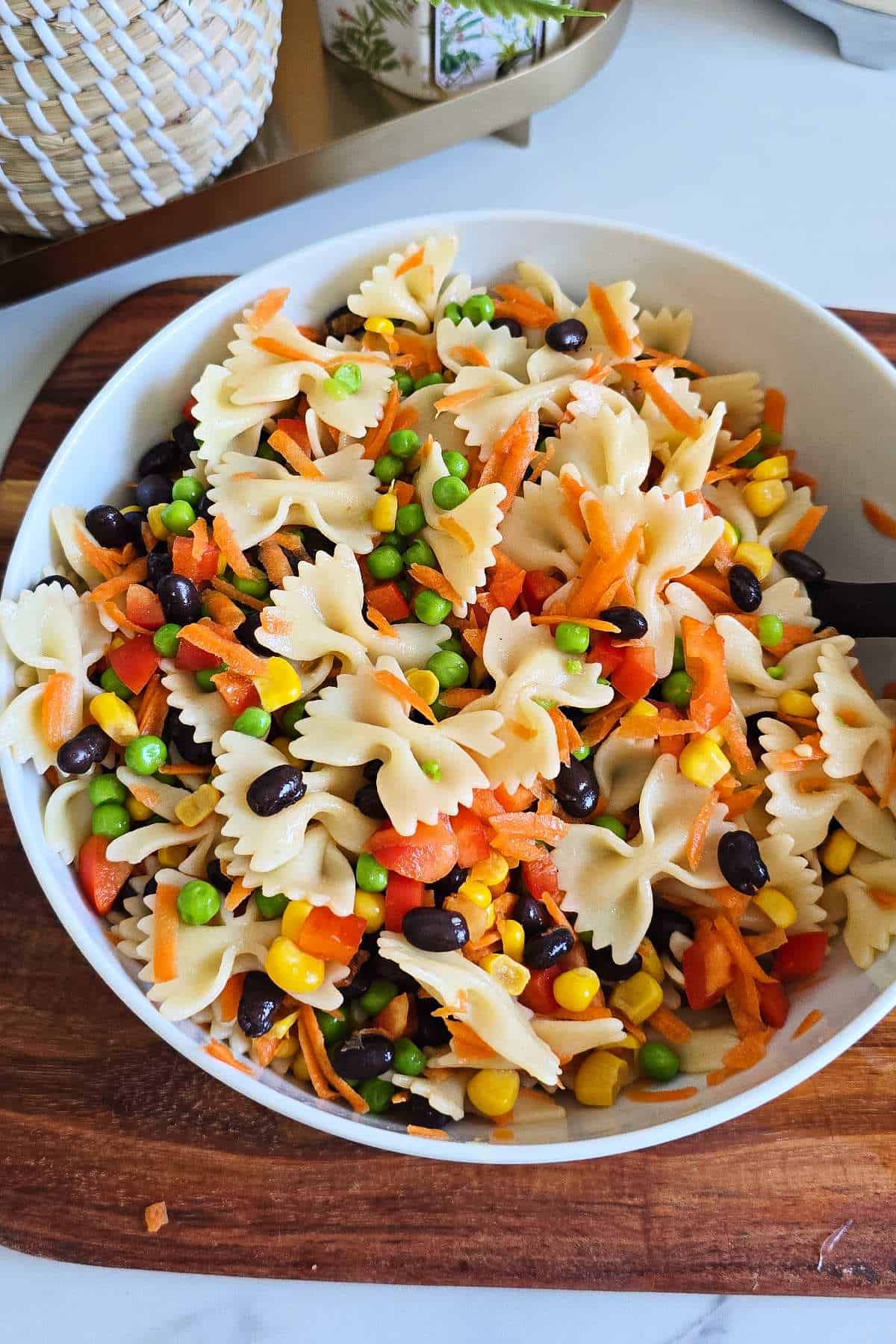 Bow tie pasta salad with peas, carrots, black beans, sweet corn, and diced bell pepper in a large bowl.
