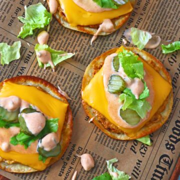 Overhead view of Chicken Big Mac smash tacos with melted cheese, lettuce, pickles, and creamy sauce on parchment paper.