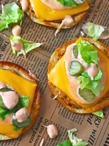 Overhead view of Chicken Big Mac smash tacos with melted cheese, lettuce, pickles, and creamy sauce on parchment paper.