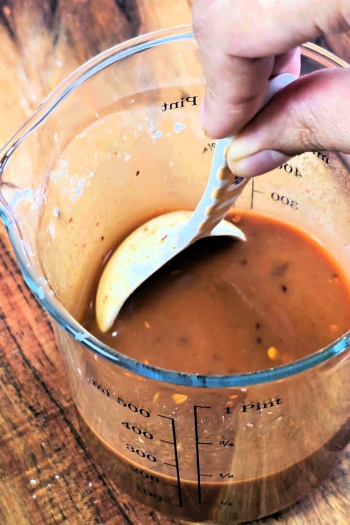 Dragon chicken sauce being stirred in a glass measuring jug with a spoon.