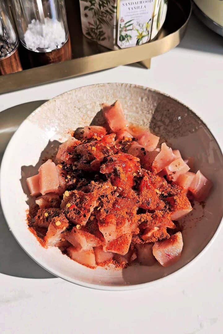 Raw chicken pieces coated in tikka spice blend and chili flakes in a bowl.