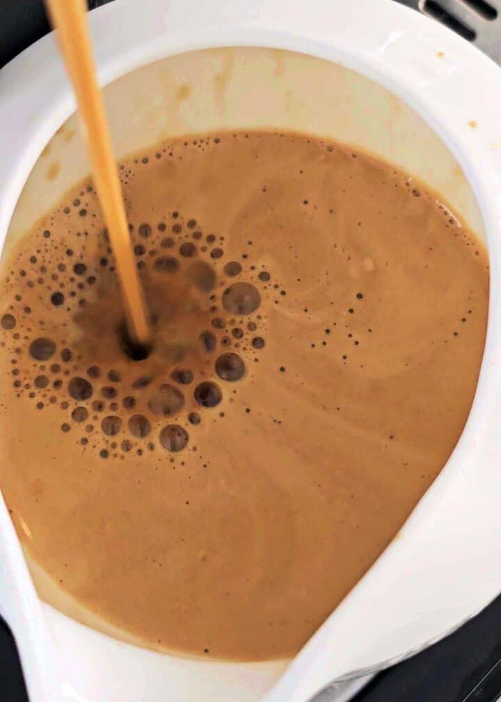 Pouring espresso into a white pitcher.