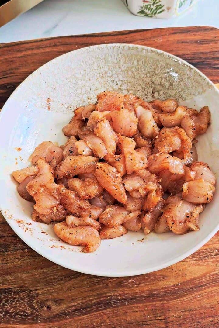 Cubed chicken seasoned with spices in a white bowl.