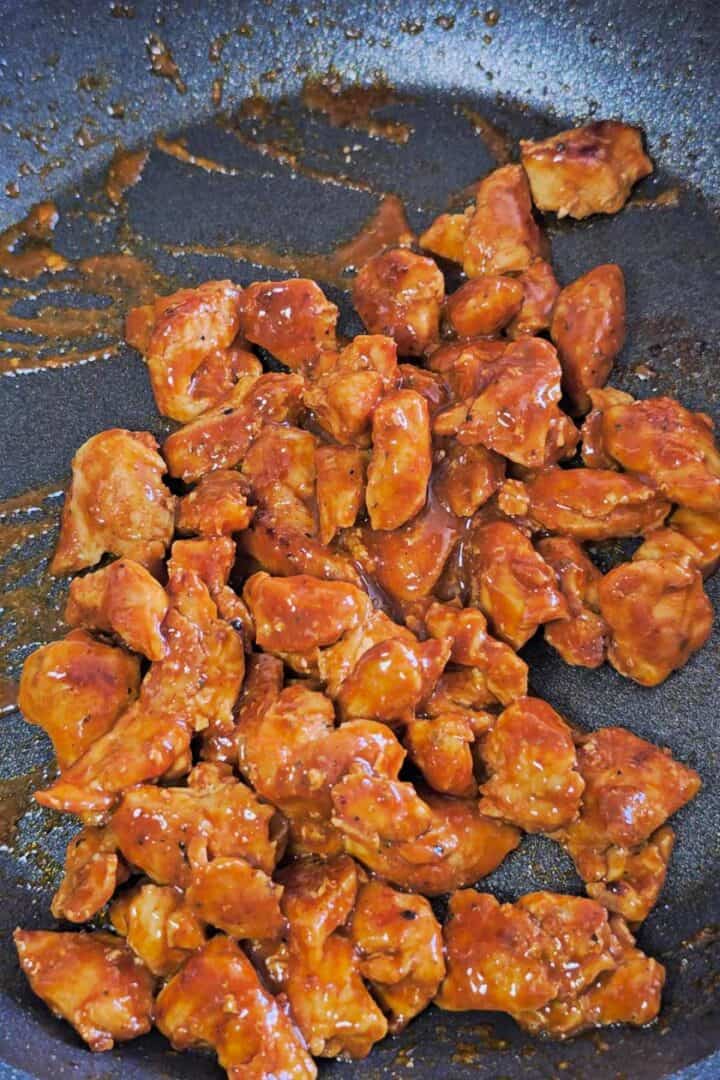 Cooked chicken coated in buffalo sauce in a skillet.