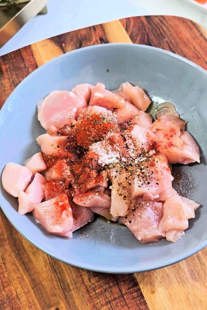 Cubed chicken in a bowl seasoned with cornstarch, black pepper, cayenne pepper, salt, and soy sauce.