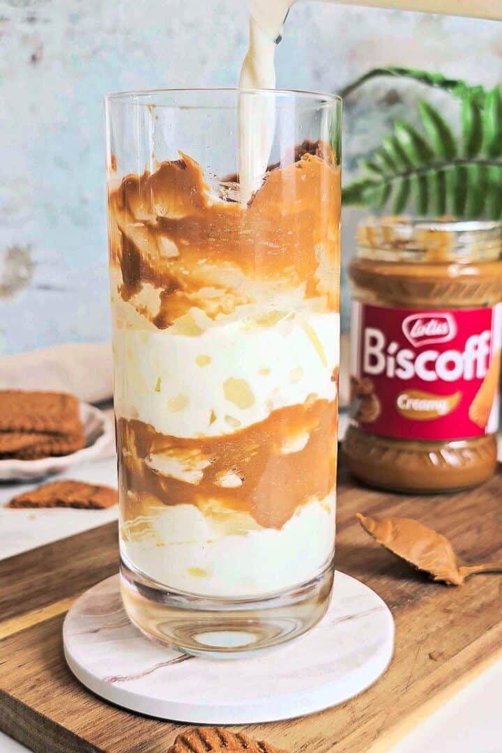 Milk being poured over ice into a glass coated with Biscoff spread.