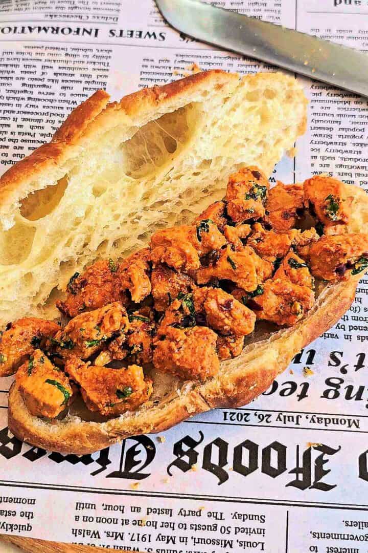 Open croissant filled generously with tikka chicken on a newspaper liner.