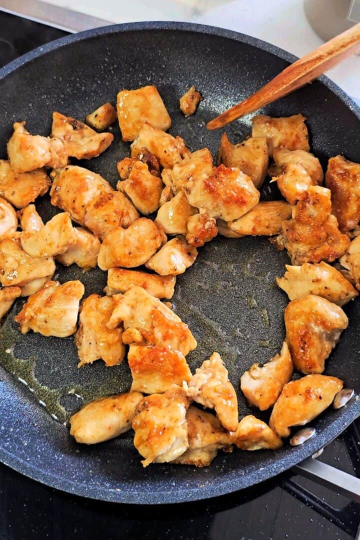 Marinated chicken pieces cooking in a skillet until lightly golden.