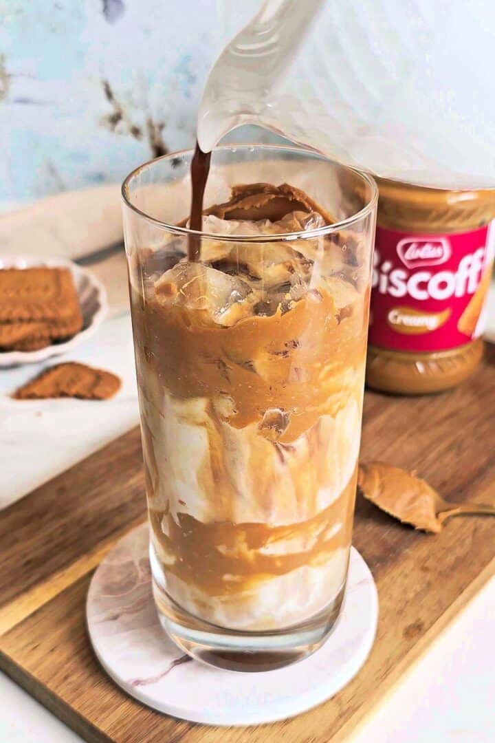Espresso being poured over ice and milk in a Biscoff-coated glass.