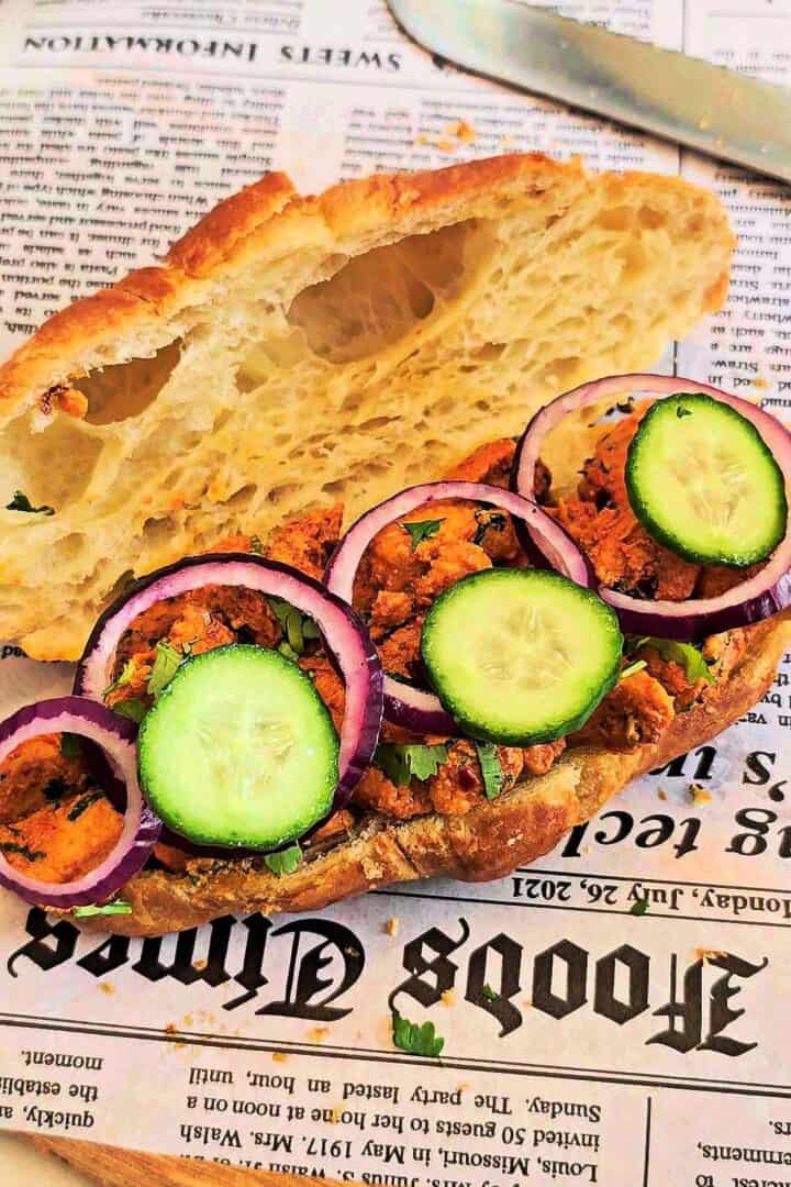 Open croissant filled with tikka chicken and topped with cucumber slices and red onion rings.