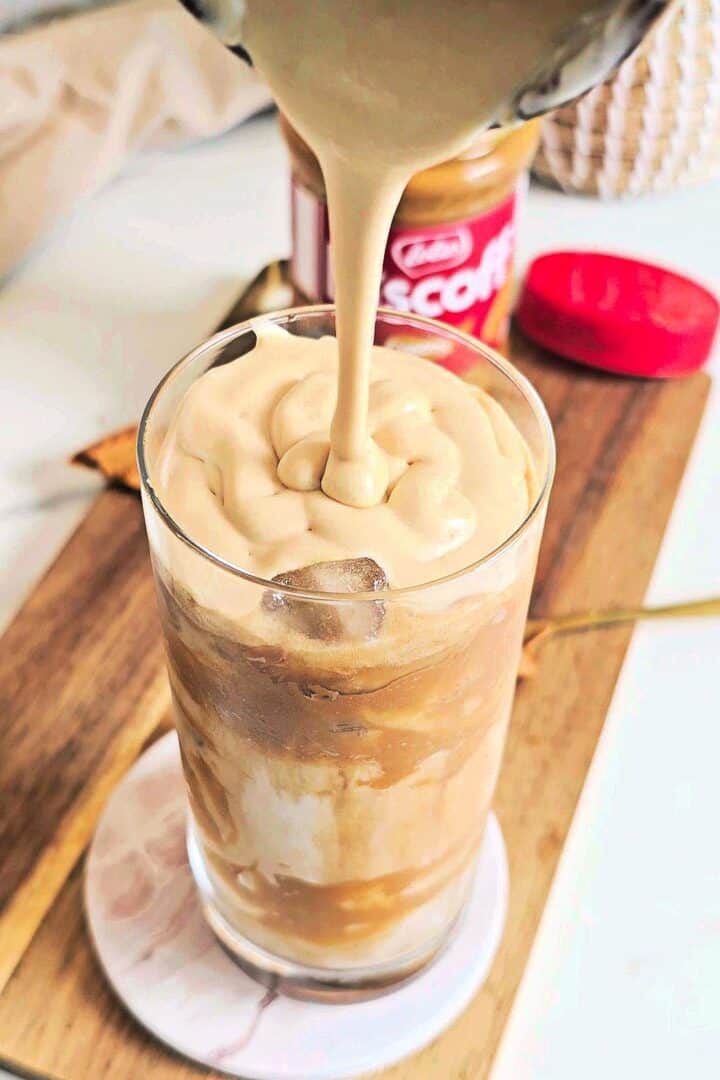 Cold foam being poured over an iced Biscoff latte.