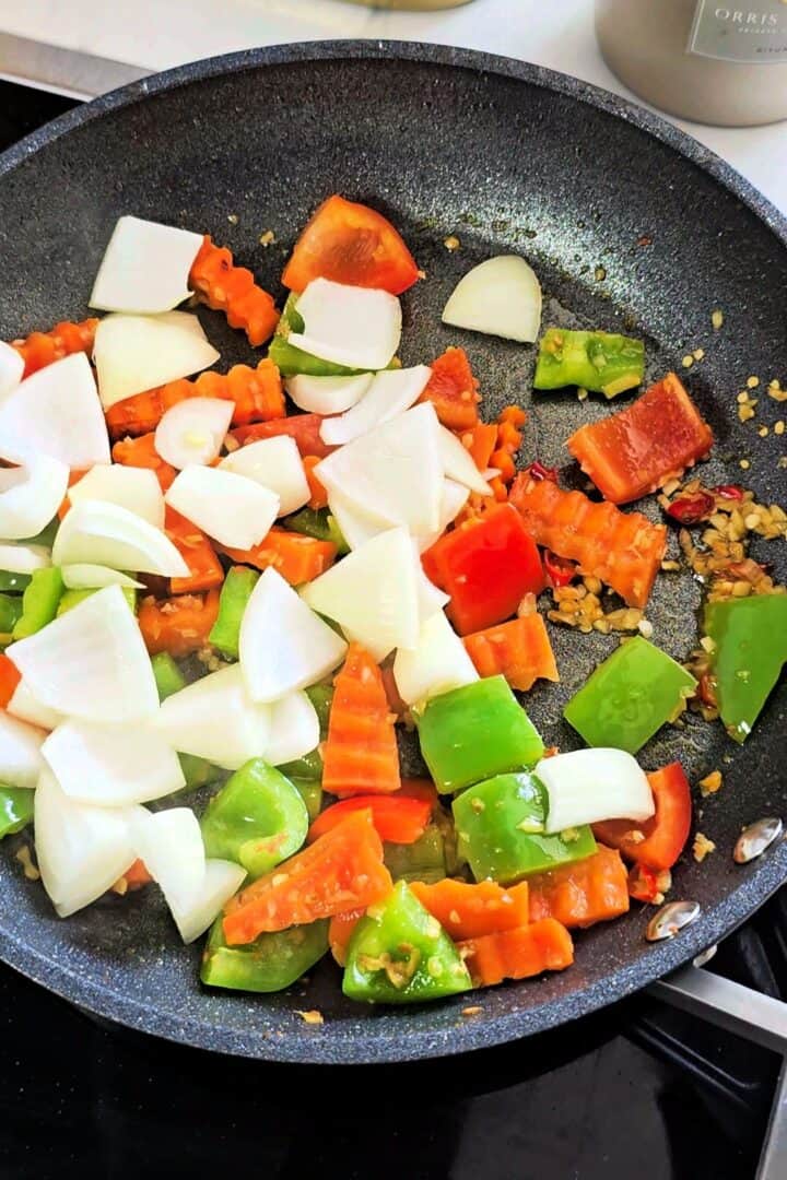 Bell peppers, onions, crinkle-cut carrots, garlic, ginger, and chilies stir-frying in a skillet.