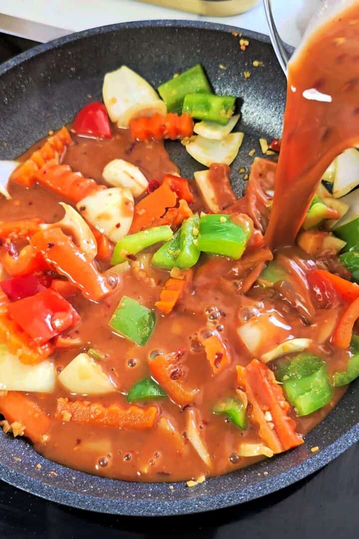 Dragon chicken sauce being poured into a skillet with stir-fried vegetables.