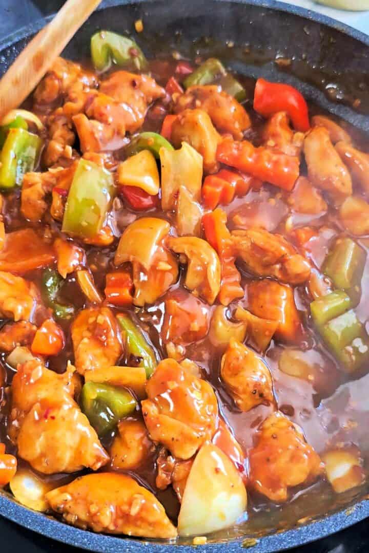 Dragon chicken simmering in a glossy spicy sauce with bell peppers, onions, and crinkle-cut carrots.