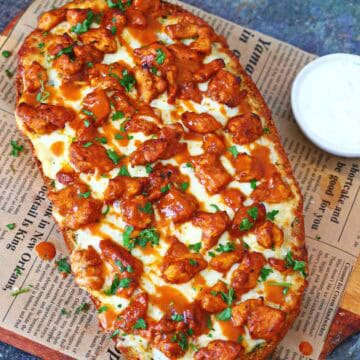 Buffalo chicken garlic bread topped with melted mozzarella, buffalo chicken, buffalo sauce, and chopped parsley on a wooden board.