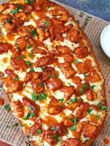 Buffalo chicken garlic bread topped with melted mozzarella, buffalo chicken, buffalo sauce, and chopped parsley on a wooden board.