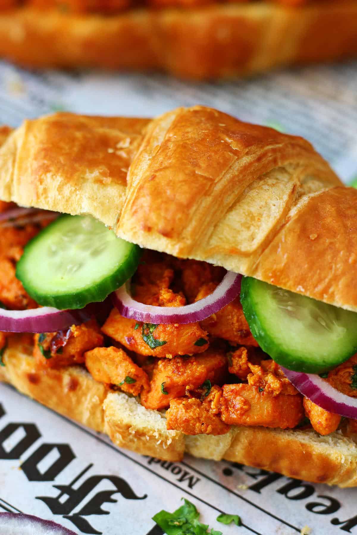 Close-up of a chicken tikka croissant packed with spiced chicken, cucumber and red onion.