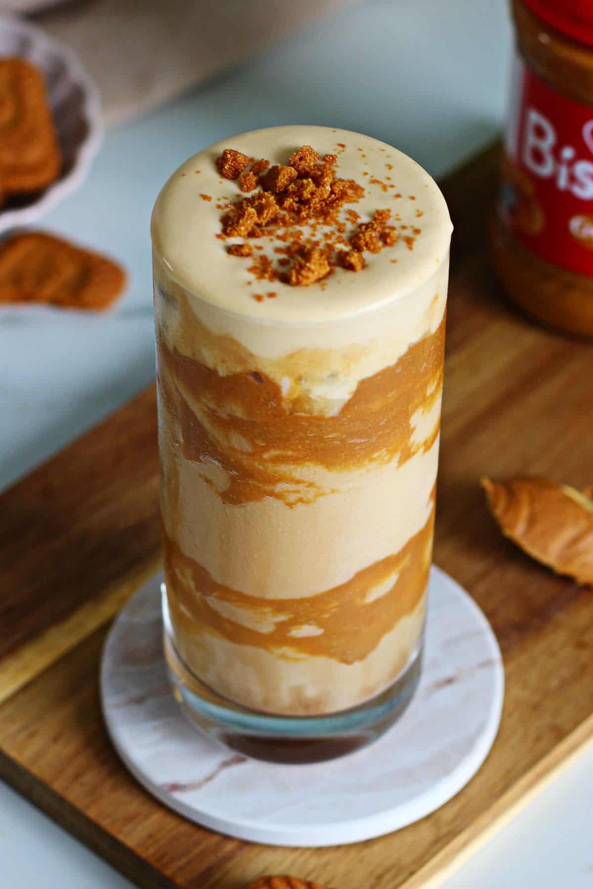 Iced Biscoff latte with Biscoff cold foam and cookie crumble in a tall glass on a marble coaster.