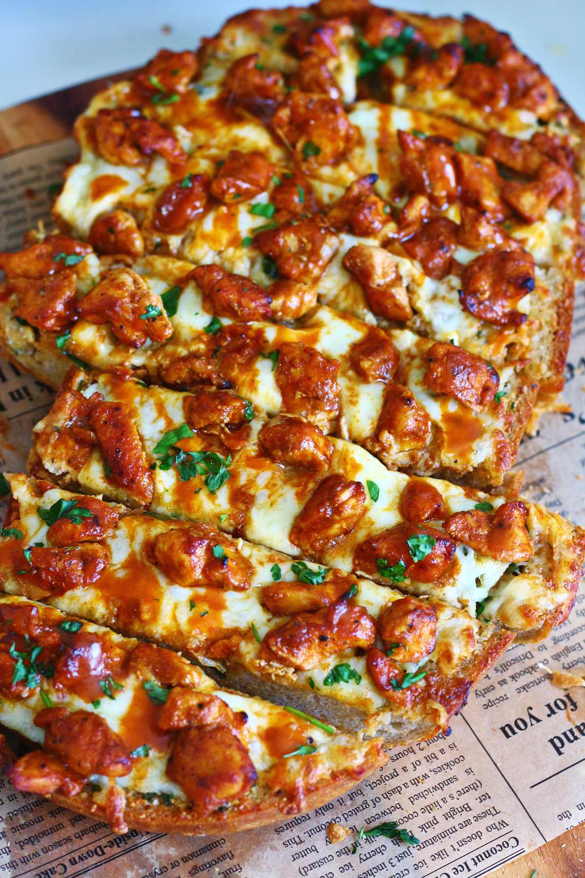 Sliced buffalo chicken garlic bread topped with melted mozzarella, buffalo chicken, buffalo sauce, and chopped parsley.