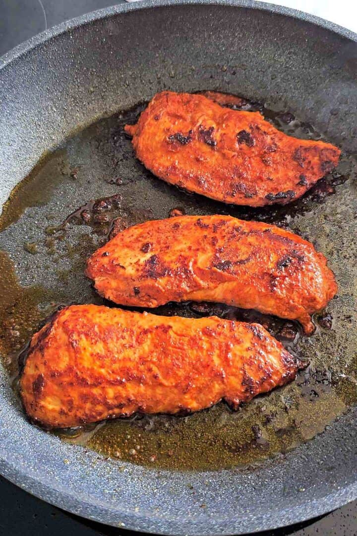 Cooked tandoori chicken pieces in a skillet with sliced onions and fresh cilantro.