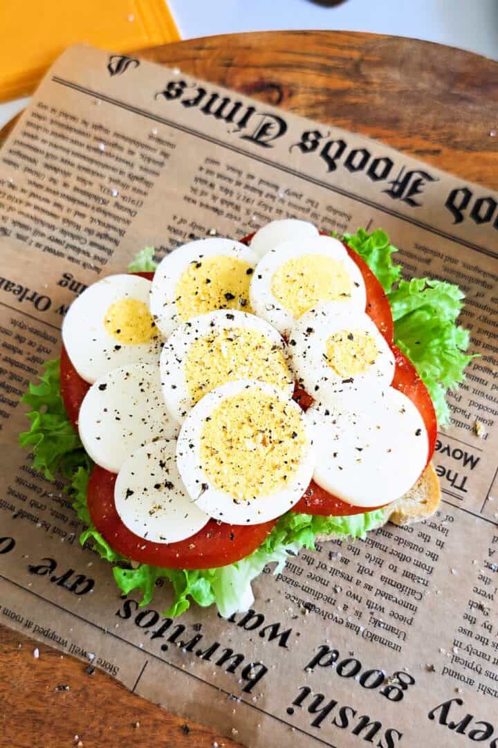 Toast layered with lettuce, tomato, sliced boiled eggs, and black pepper.